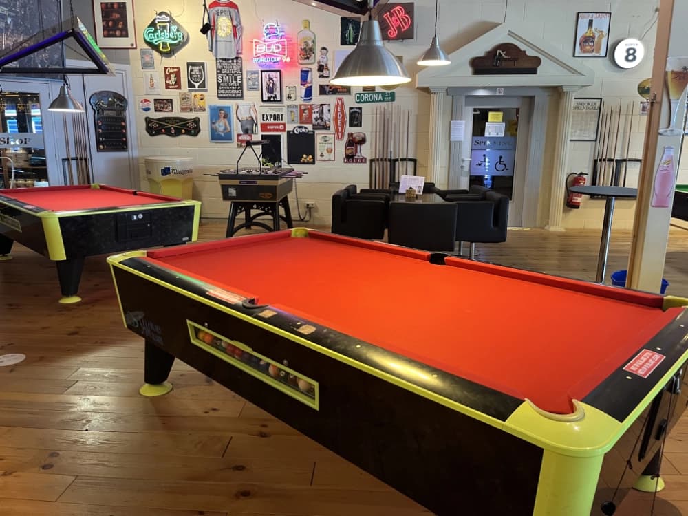 Twee pooltafels met op de achtergrond een kickerkast en een snookertafel.